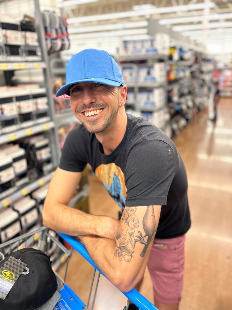 Frank Brown Cloud pushing a shopping cart through Walmart while wearing an as-yet-unpurchased blue hat